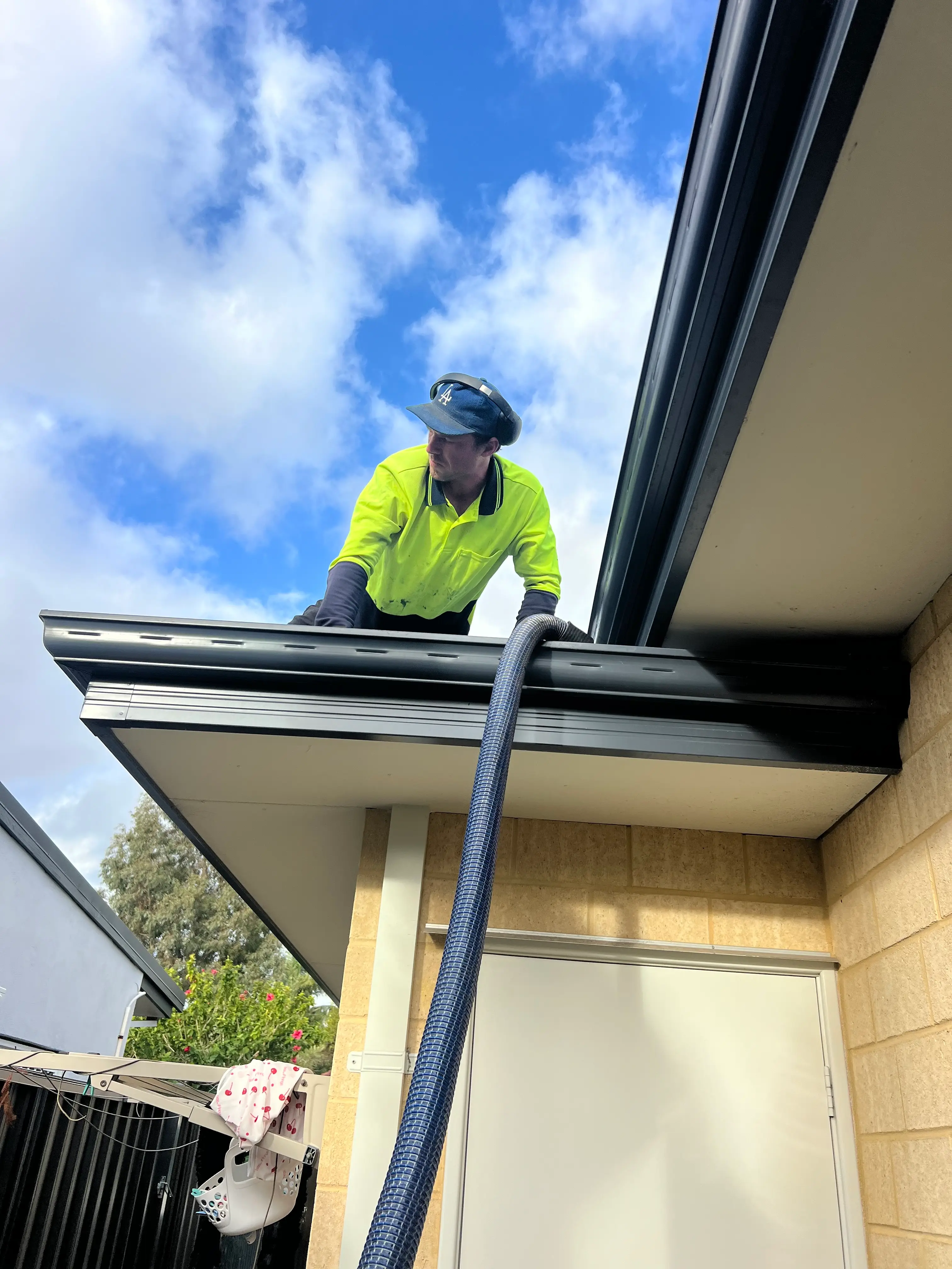 Worker in high-visibility clothing cleaning a roof gutter with a vacuum hose