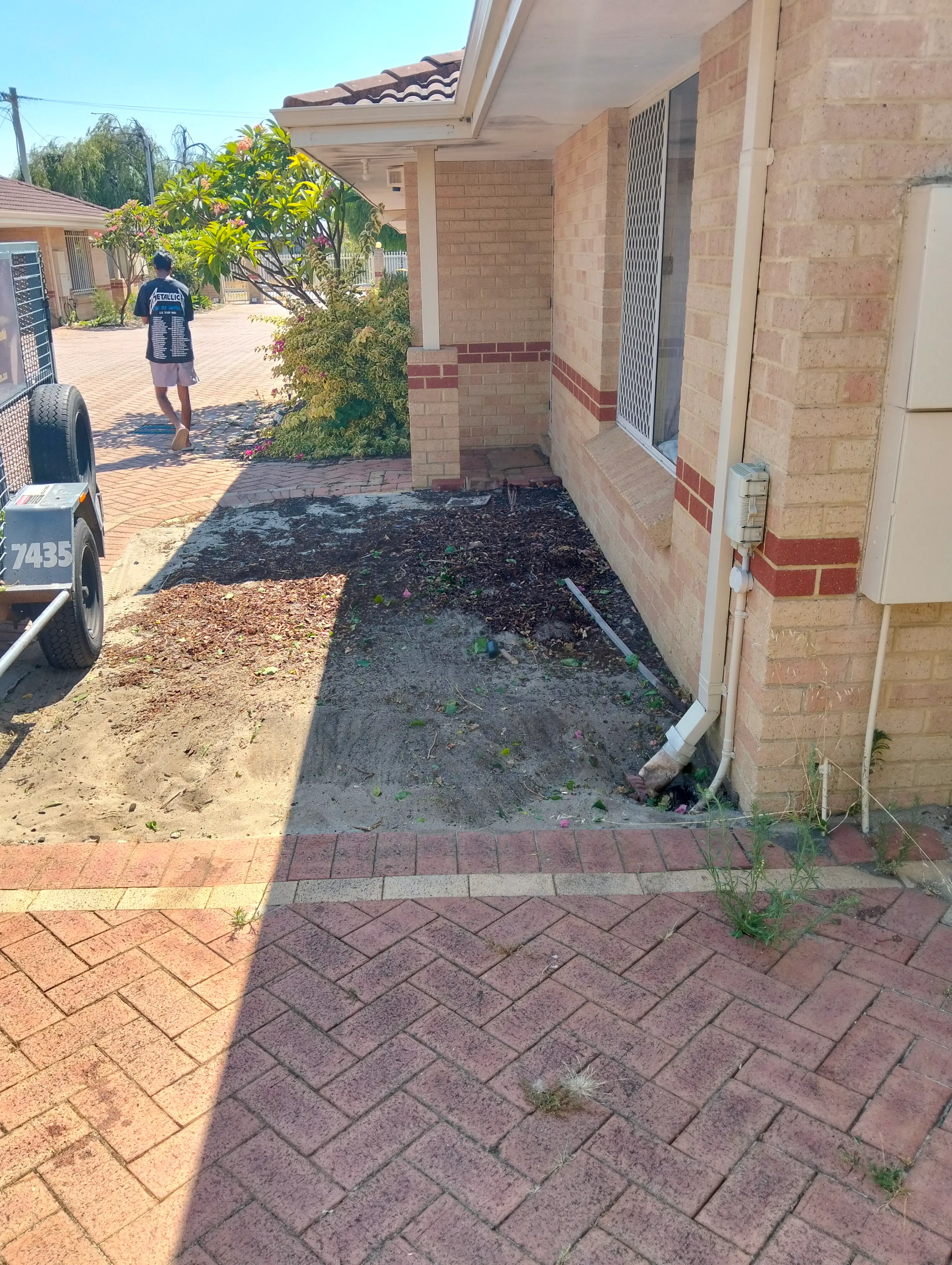 Same garden area with exposed soil beside the brick home and paved path
